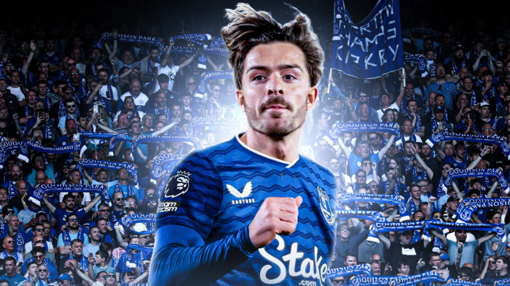 Jack Grealish wearing an Everton shirt in front of a backdrop of Toffees fans.