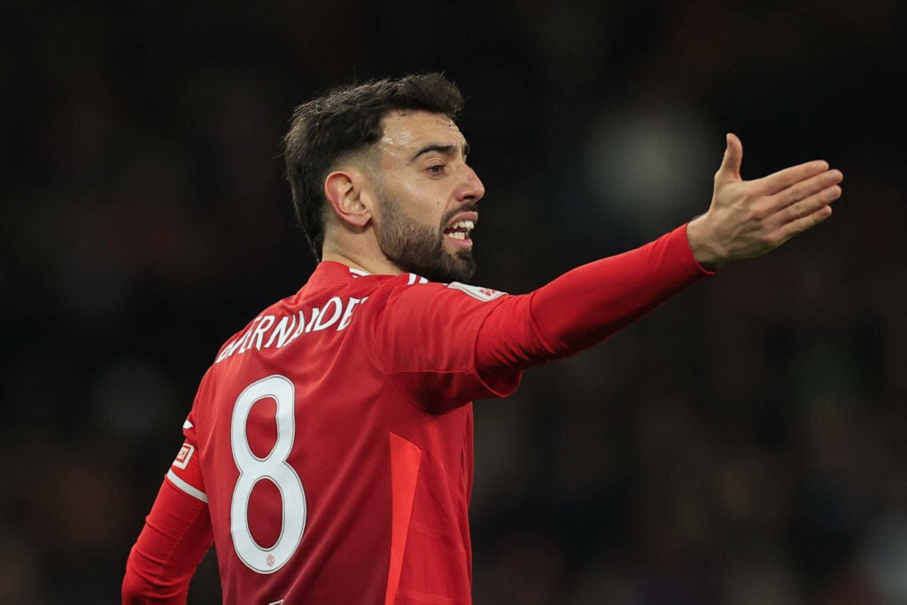 Bruno Fernandes playing for Manchester United, holding his right arm aloft as he remonstrates with officials.