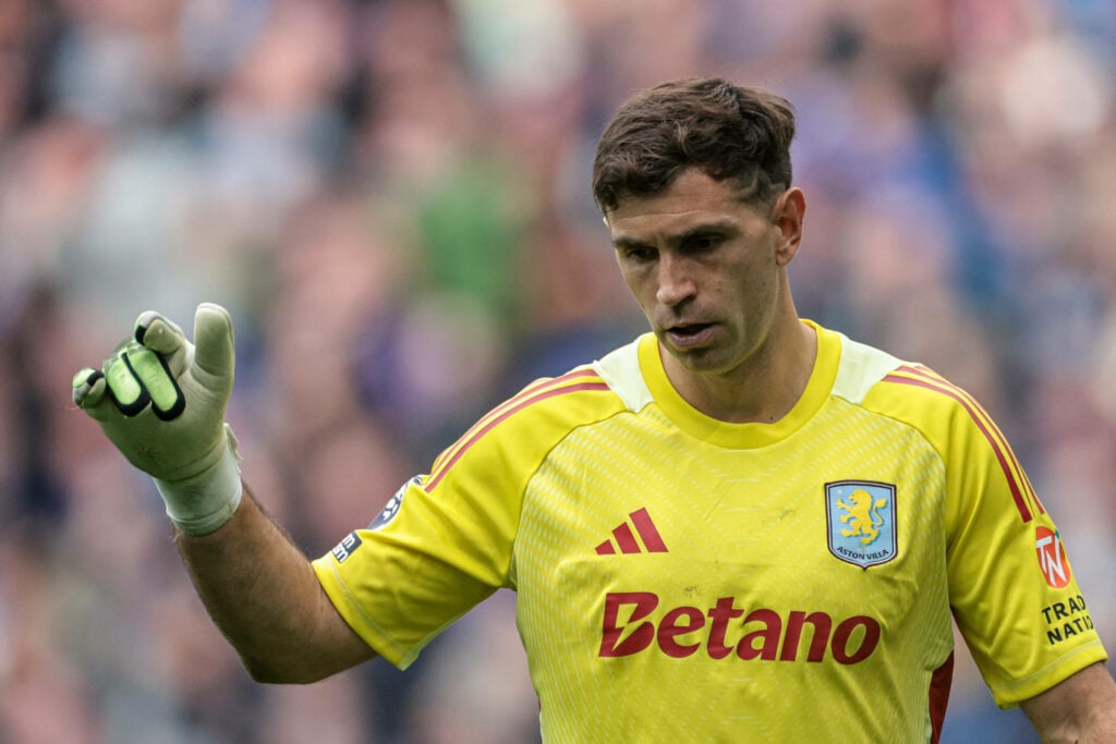 Emiliano Martinez looking to the ground focused whilst holding his right arm in the air