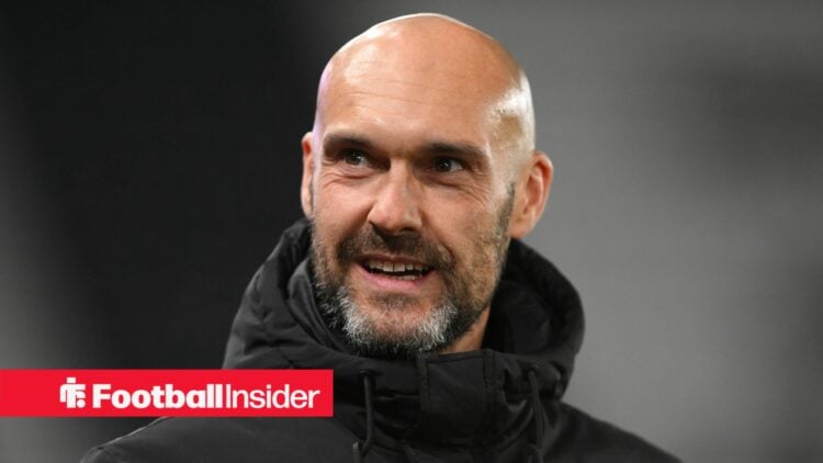 Peterborough United manager Luke Williams smiles while standing on the touchline.
