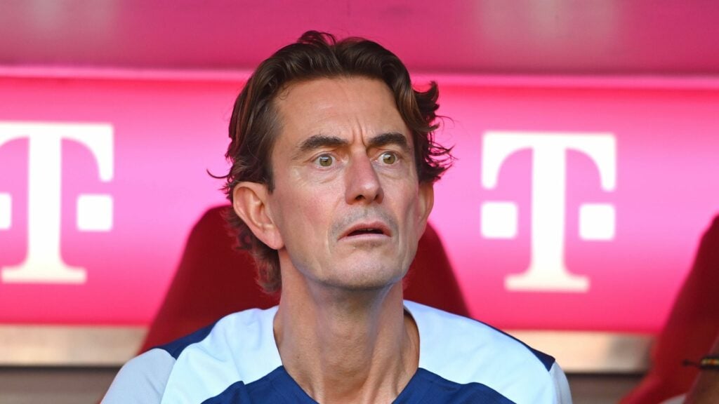 Tottenham manager Thomas Frank sits in the dugout with a surprised expression on his face.