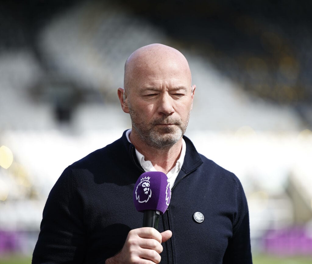 Alan Shearer stands holding a Premier League microphone.