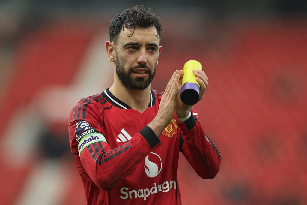 Manchester United midfielder Bruno Fernandes applauds while holding the Player of the Match trophy after a game.