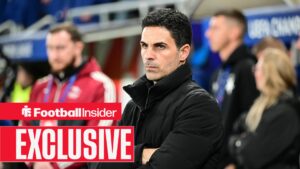 Football Insider exclusive as Arsenal manager Mikel Arteta stands looking stern with his arms folded.